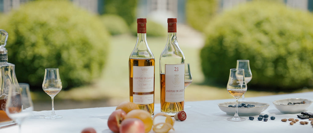Photo de deux bouteilles de abs Armagnac du château de Lacquy sur une table de jardin accompagné de fruit. 